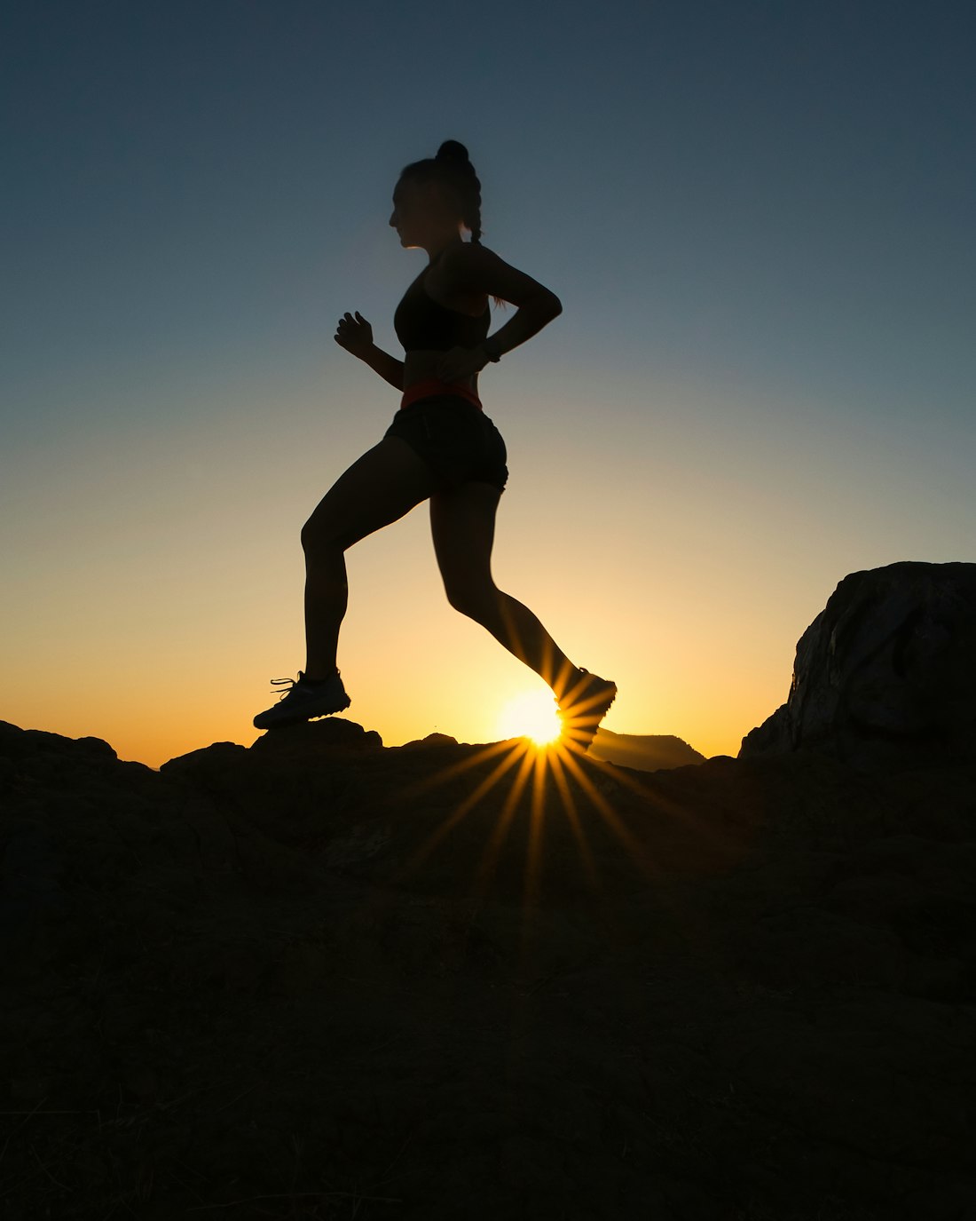 A runner in silhouette striding uphill into a bright sunrise